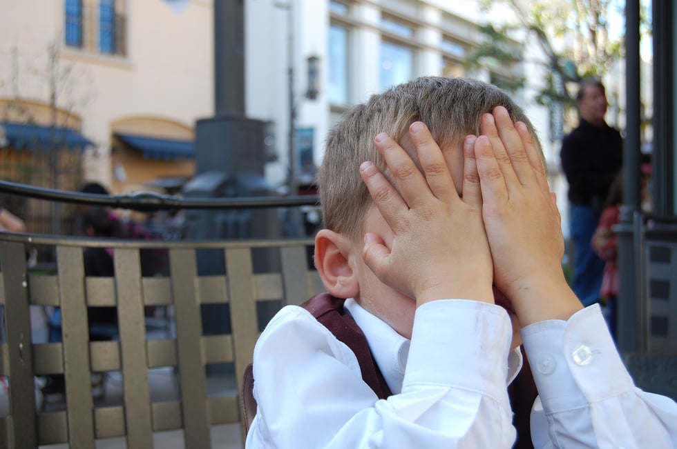 boy in city covering his face with his hands