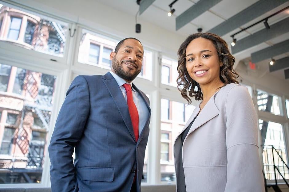 male and female business people standing in front of window smiling