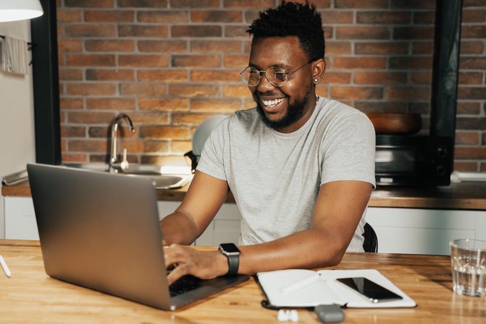 man smiling and typing on a laptop in kitchen